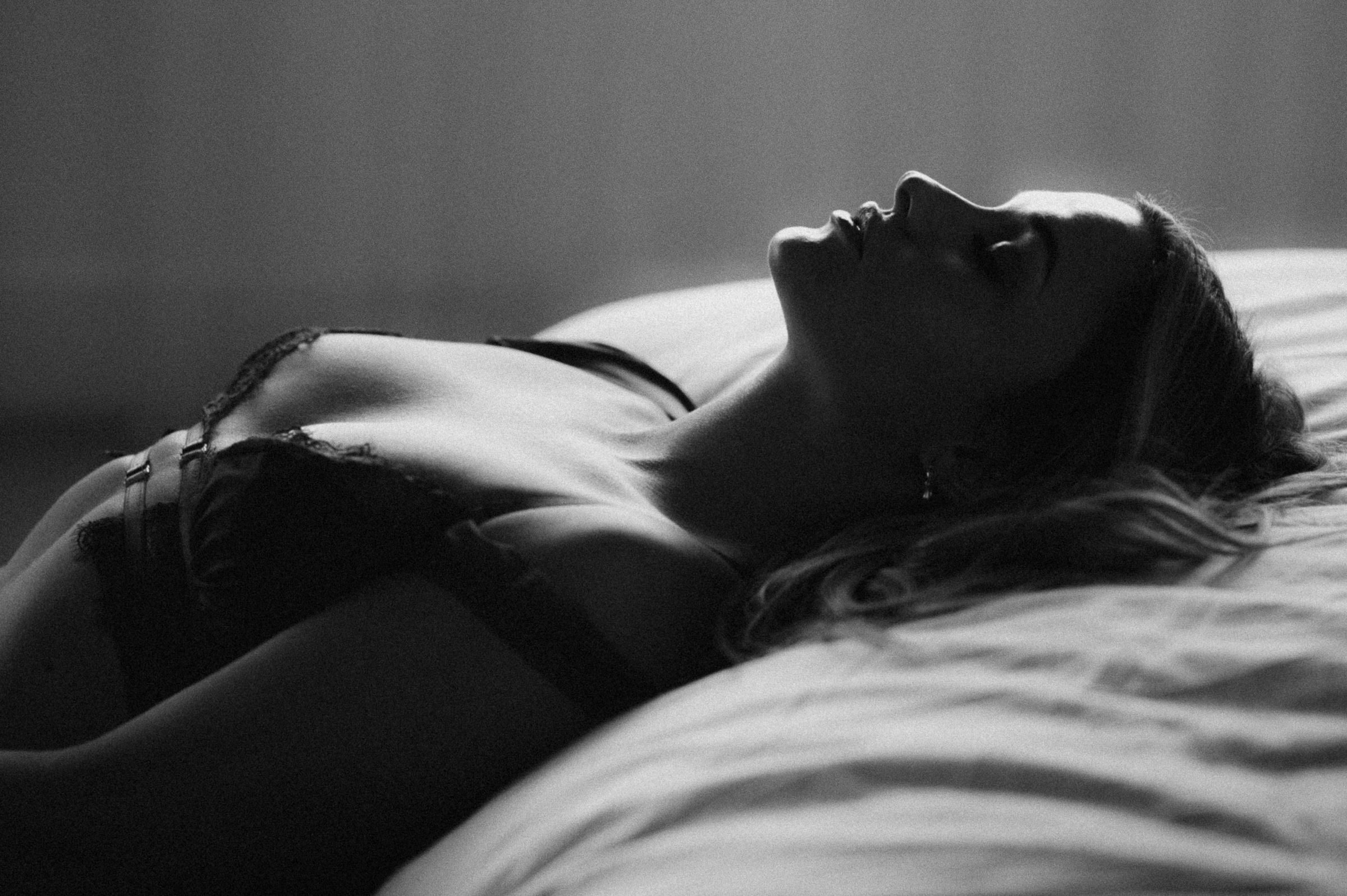 Black and white boudoir portrait of a woman reclining on a bed, softly lit to highlight calm presence and intimacy in a Phoenix boudoir photography session