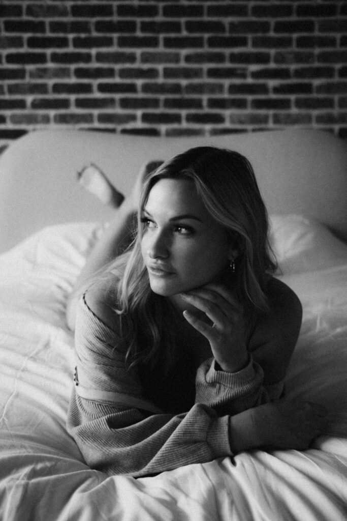 Phoenix boudoir photography portrait of a woman lying on a bed with soft natural light and a relaxed, intimate pose.